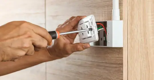 Electrician using a screwdriver to install a power outlet